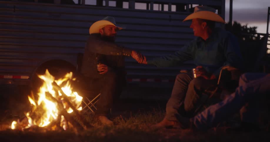Two men shaking hands sitting in front of a bonfire