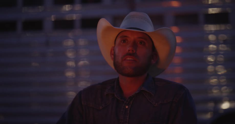 Man in cowboy hat sit with face illuminated by amber glow