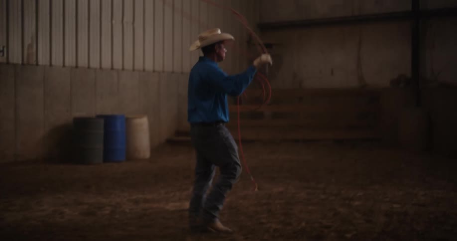 Man removing his rope from the horns of a bucking bull and throwing it again