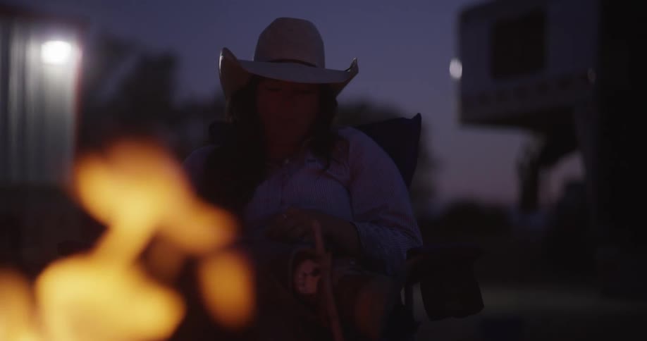 A woman with cowboy hat is eating something while there is a flame of fire in front of her