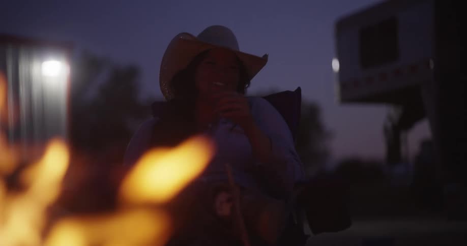 Cowgirl sits in front of a campfire at night