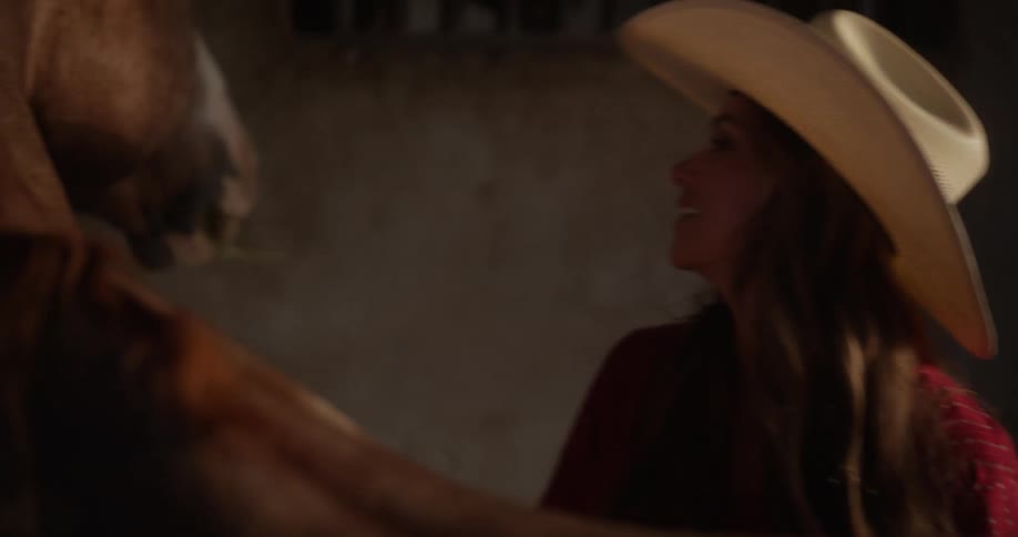 A woman in a stable caring for a horse while wearing a cowboy hat