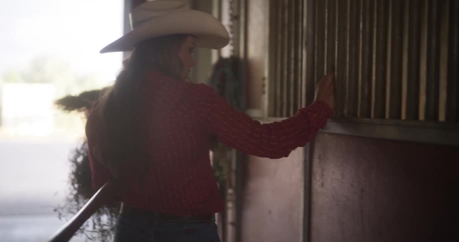 Cowgirl feeds hay to a horse in a stable