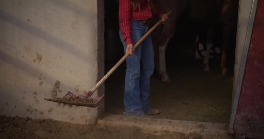 A woman is shoveling by the horse stables