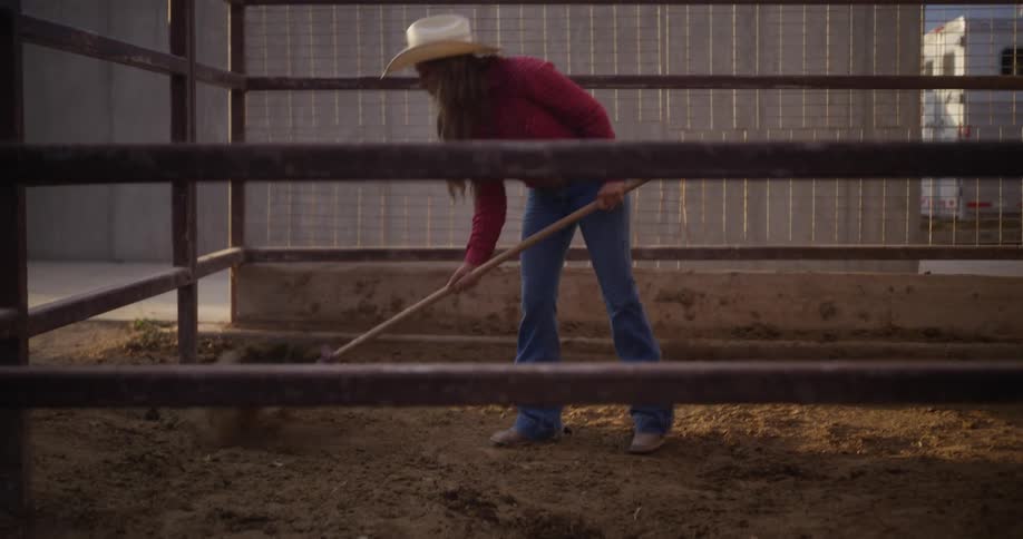 A woman wearing a cowboy hat shovels horse dung