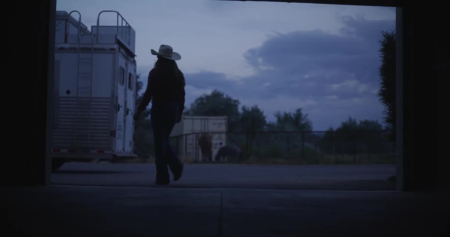Cowgirl pushing a gate up on a shed in the morning