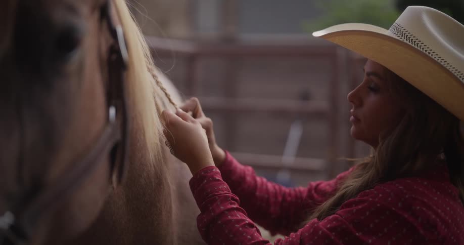 A woman with a cowboy hat is doing braids in a horses hair
