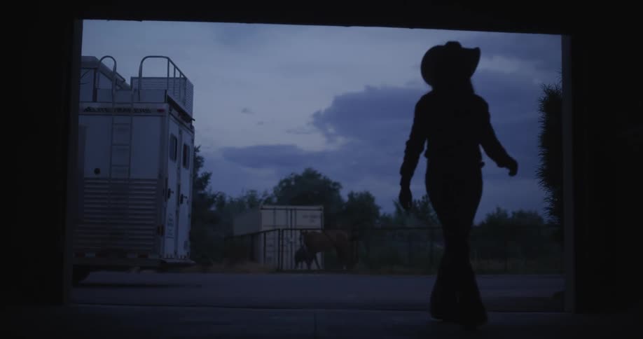 Silhouette of a cowgirl lifting a screen door at dawn