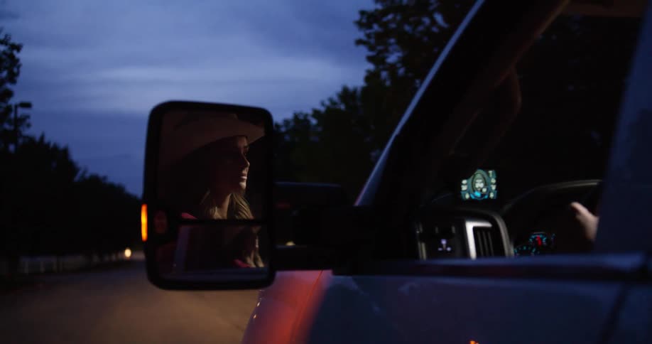 A woman is driving a truck as her reflection is seen in the side mirror