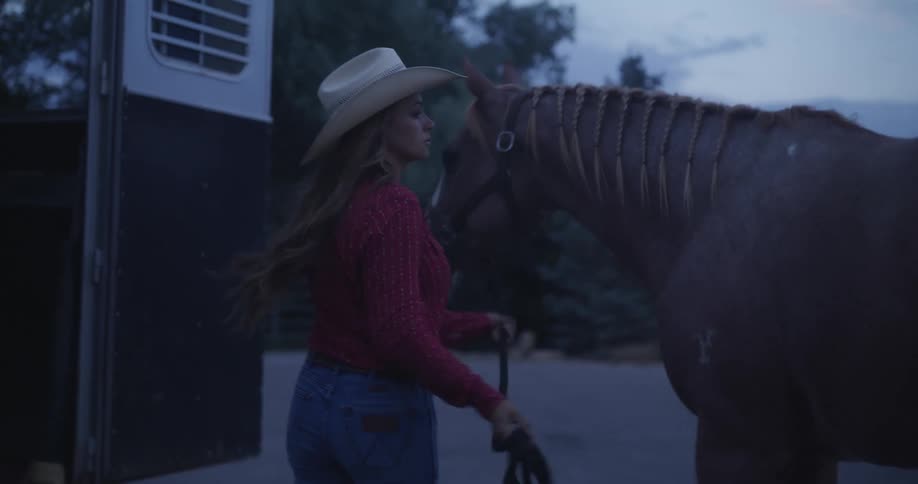 A woman in a hat placing a horse in the back of a vehicle