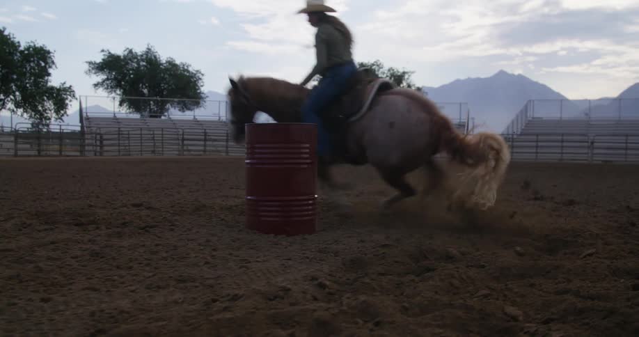 Cowgirl rides a horse around a red barrel in the rodeo
