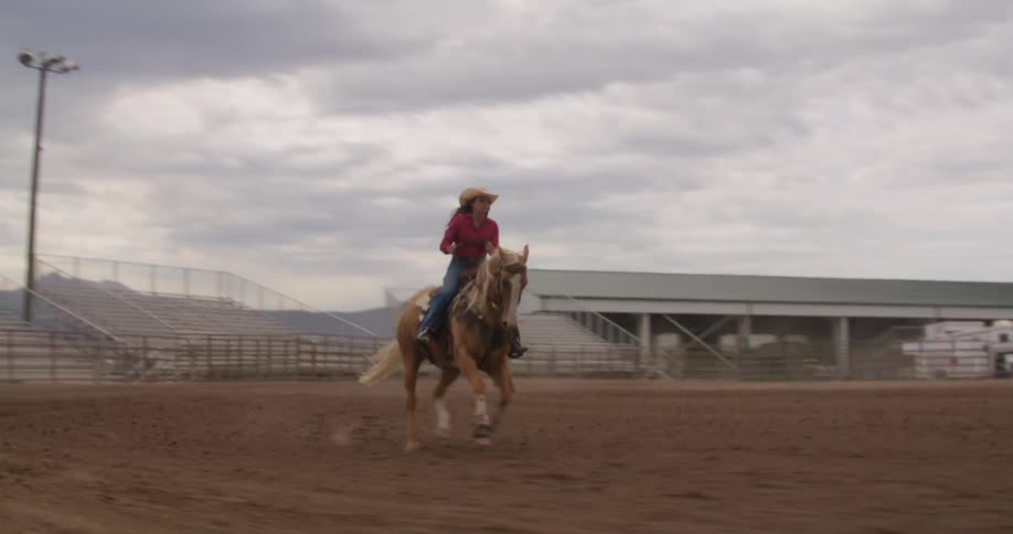 Woman on top of a horse riding in a sandy field