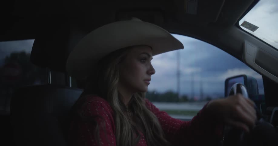 A blonde woman with cowboy hat driving a car
