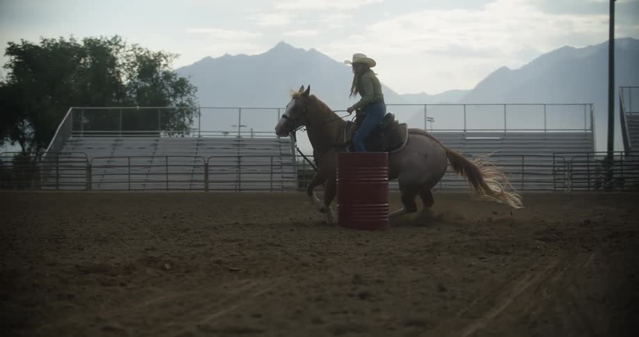Cowgirl rides a horse around a red barrel in the rodeo