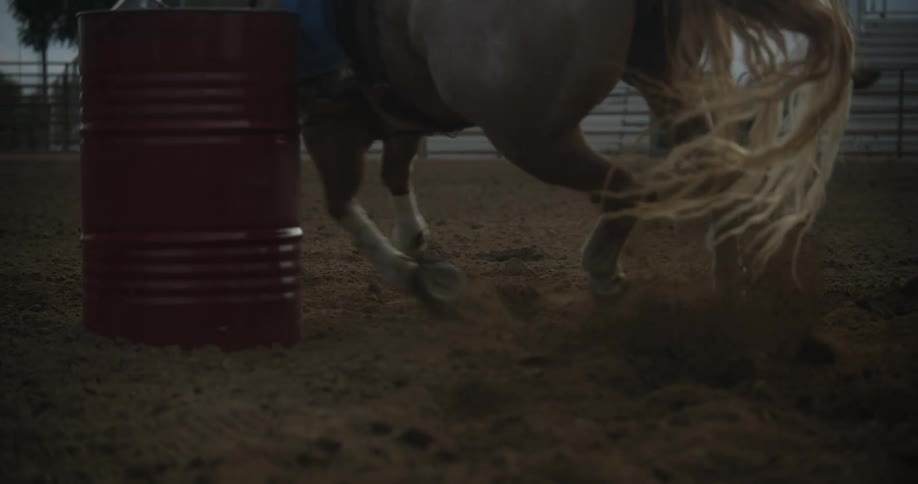 A horse running around a metal barrel in an arena