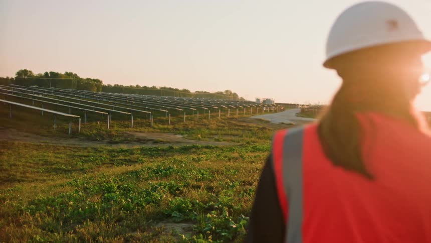 A female solar worker looks out at the panels at sunset