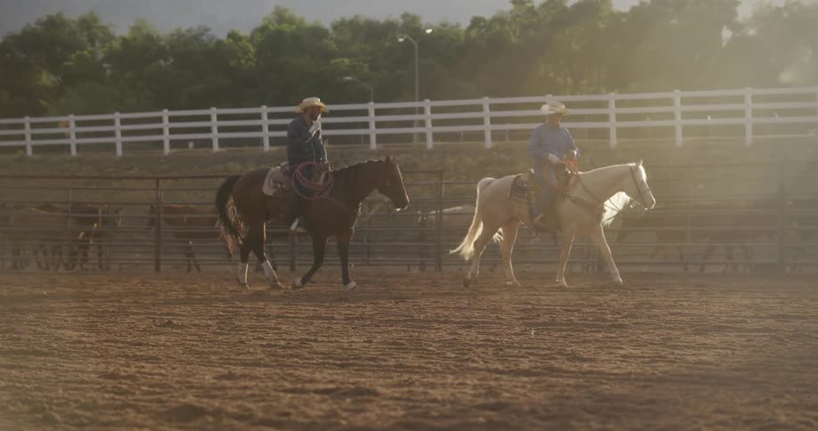 Two men riding horses on a ranch with bright sunlight coming from the sky