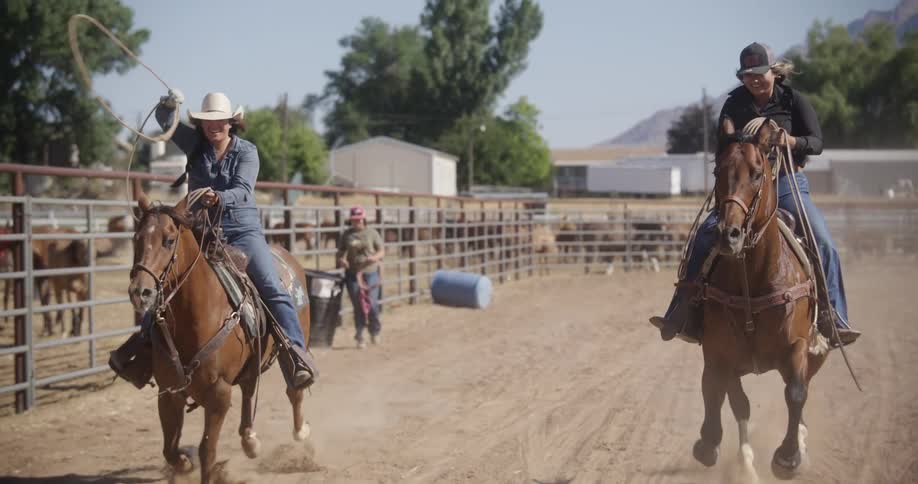 Two women on top of two horses running in a ranch