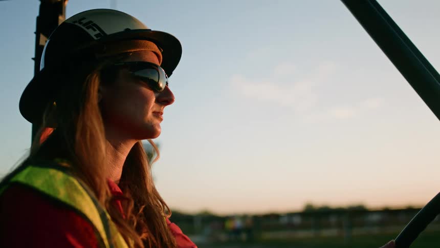 Female construction worker drives a truck at sunrise