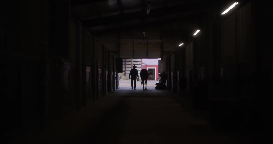 Cowboy leads a horse out of the stable