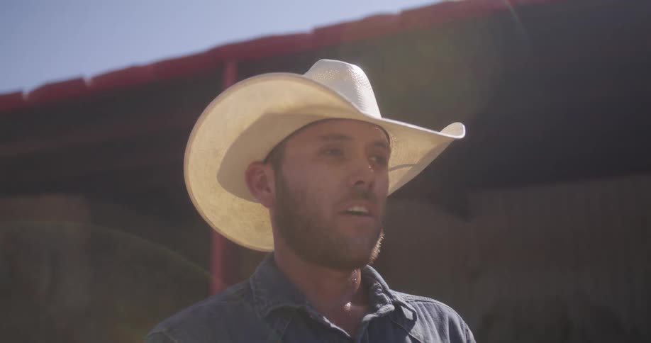 Cowboy wearing a hat stand next to the stables