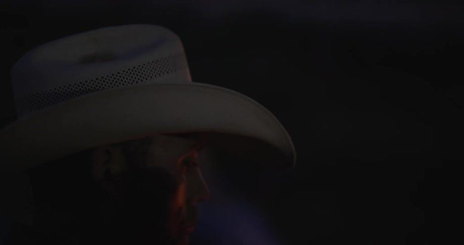 Cowboy with his back turned wearing a white hat talking at night