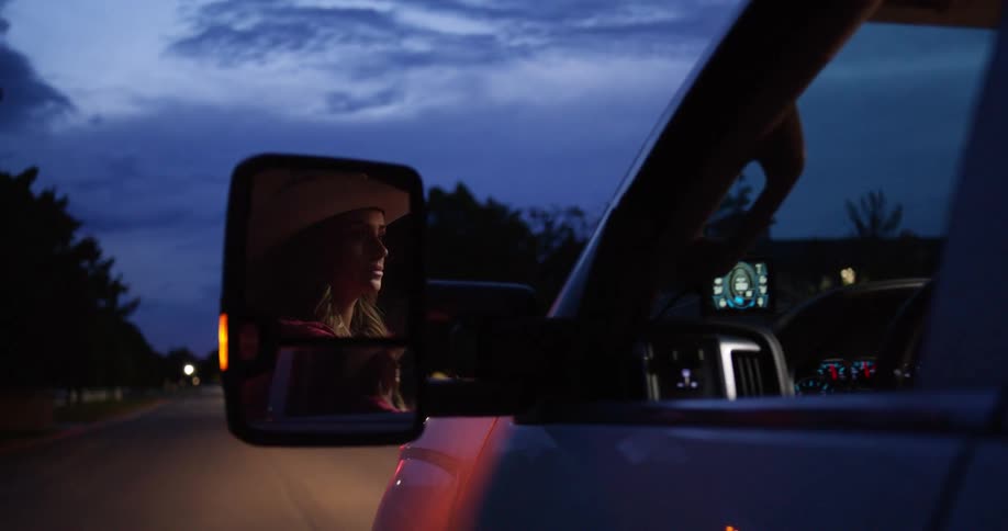 A woman is driving a truck as her reflection is seen in the side mirror