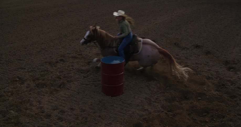 Woman riding a horse and circling a metal barrel