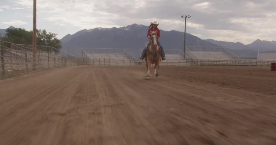 A person wearing a cowboy hat is horseback riding around a dirt track