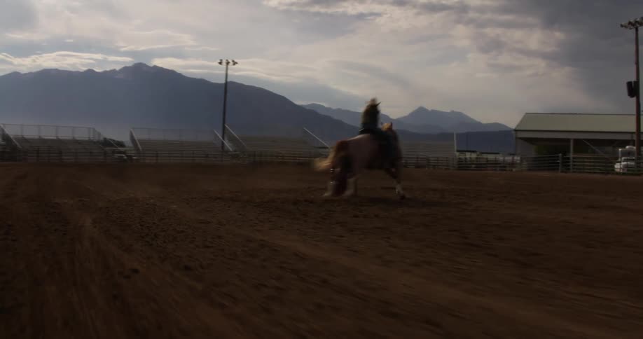 Cowgirl rides a horse around a red barrel in the rodeo