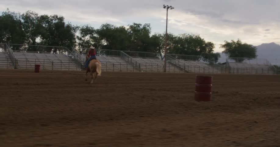Woman on top of a horse performing highspeed maneuvers around barrels in a rodeo arena