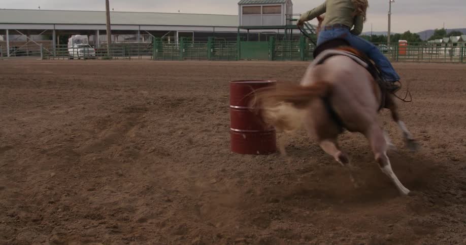 Woman riding a horse and performing a change of direction around a metal barrel in a rodeo arena
