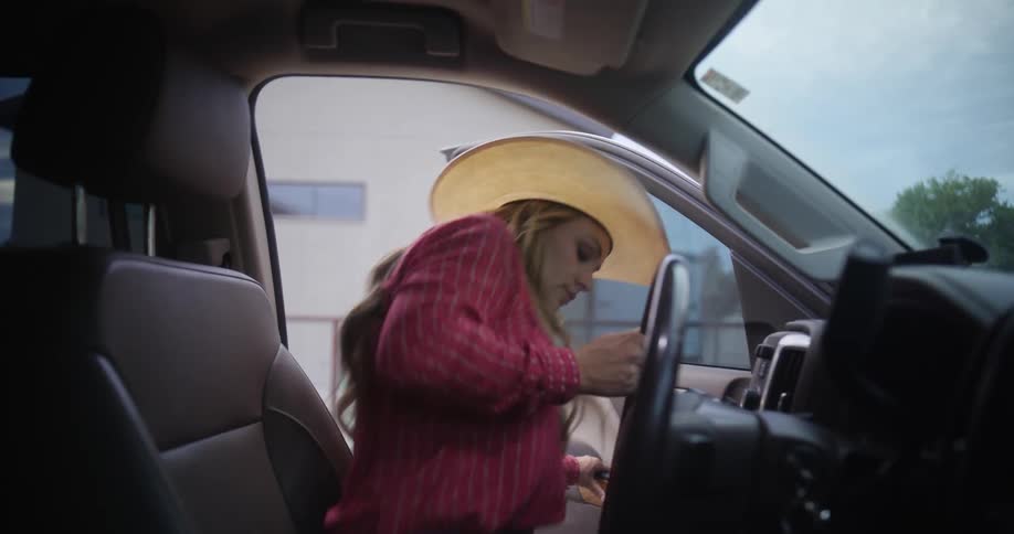 A woman wearing a cowboy hat while getting into her car