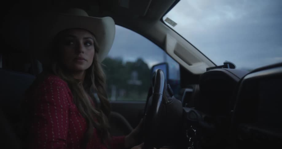 A woman is driving a truck as she looks around and moves the steering wheel as she drives