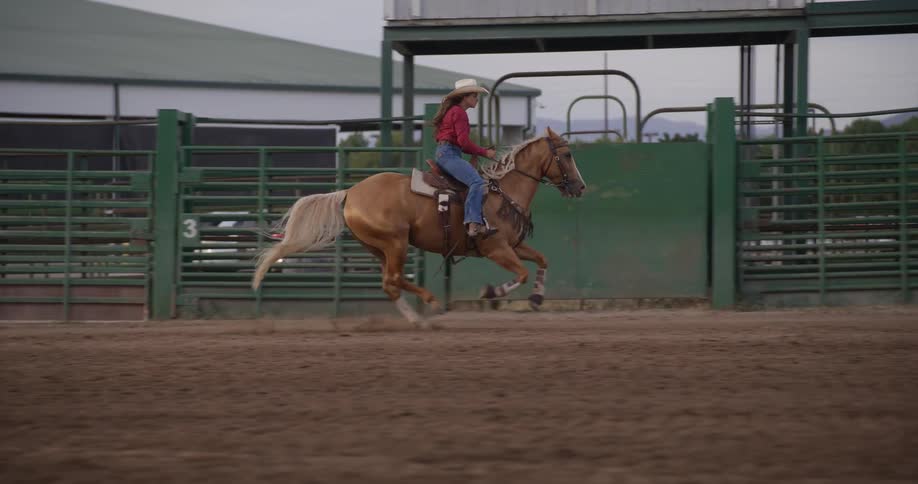 Lady on cowboy hat rides a horse in an enclosed area at midday