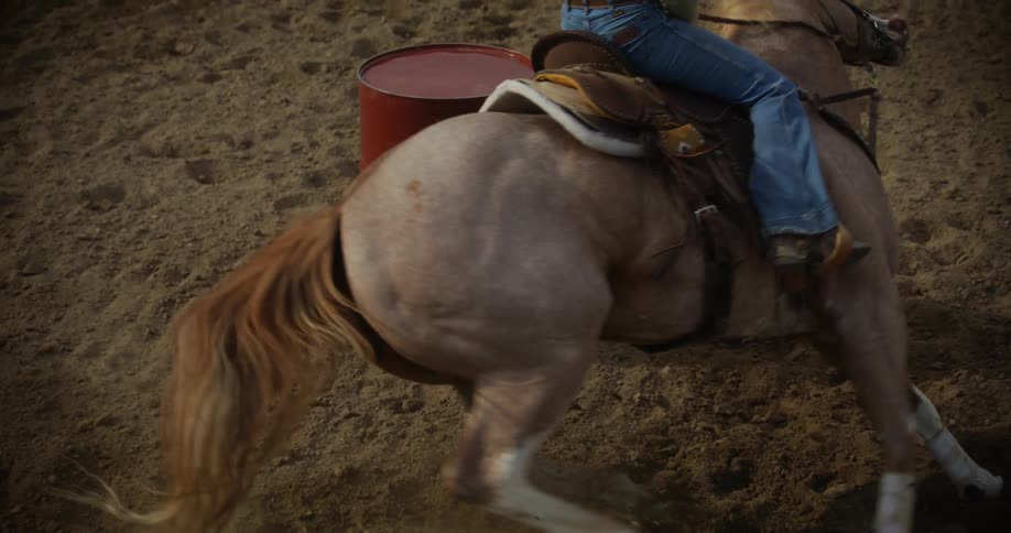 Slowmotion of a rodeo horse circling a barrel with the assistance of a woman