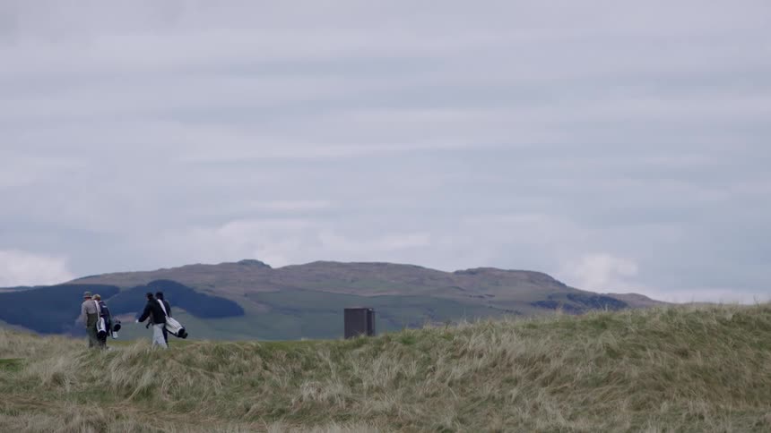 Men carrying golf bags walking on a hill at midday