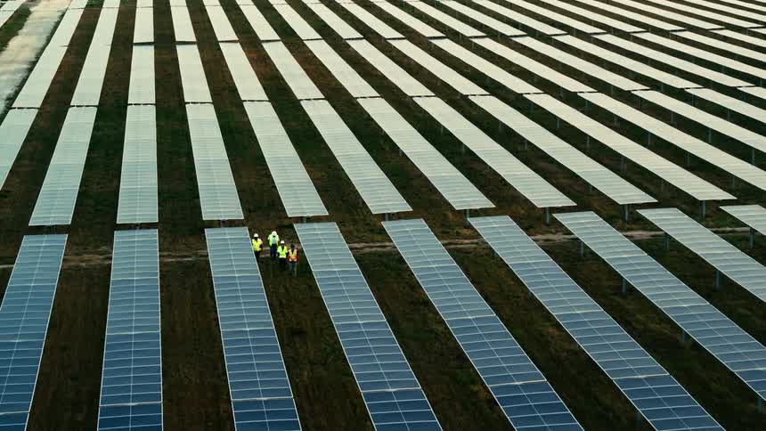 Utility workers are walking between rows. of solar panels on a solar farm