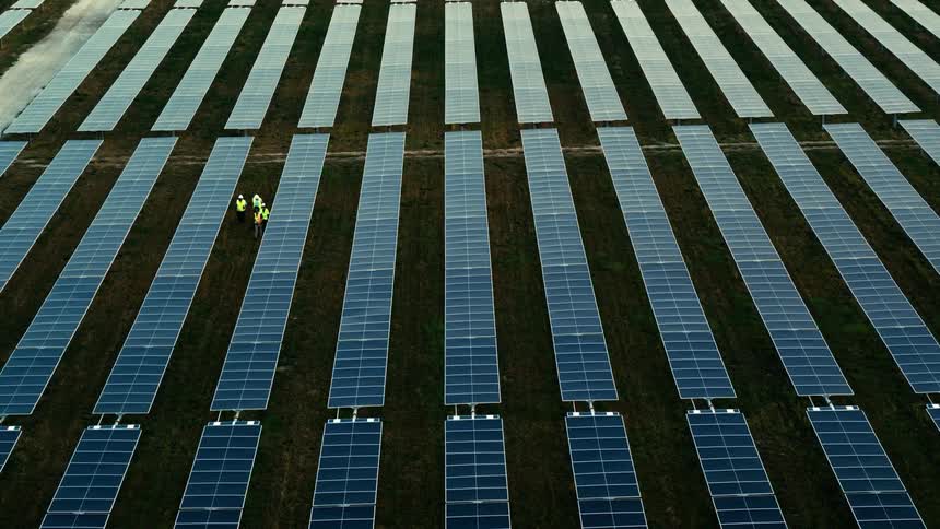 Utility workers are walking between solar panels on a solar farm