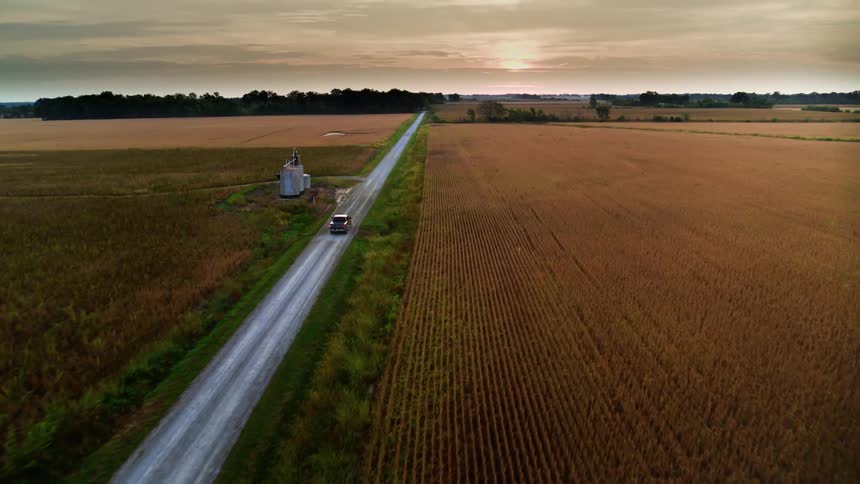 Aerial view of truck driving alongside wheat fields at sunset in American Midwest