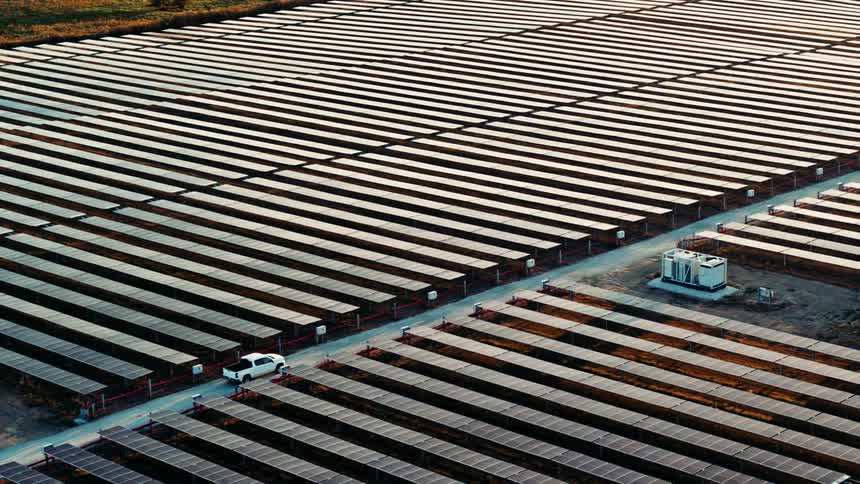 A truck driving through rows of symmetrical photovoltaic cells at golden hour