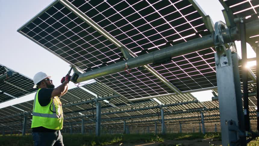 A utility worker holds a hand drill as he works on solar panels