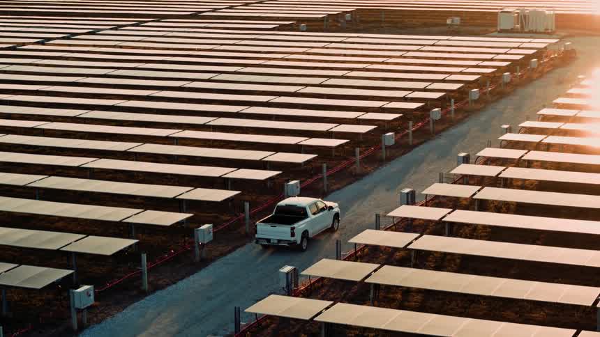 Truck driving through rows of solar panels at sunset with golden light reflecting off panels