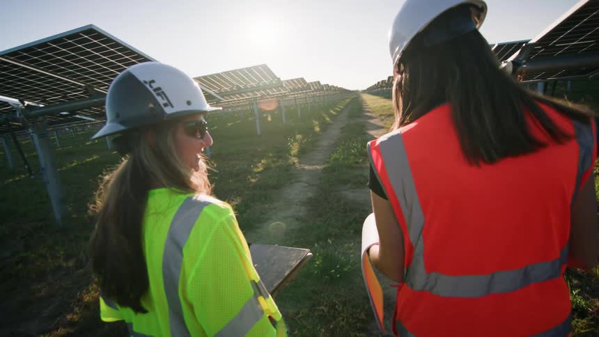 Two female solar workers walking inspecting a solar farm