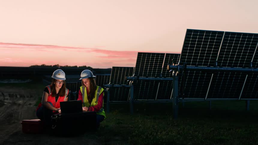 Two female construction workers wearing hard hats are working the night shift at solar field