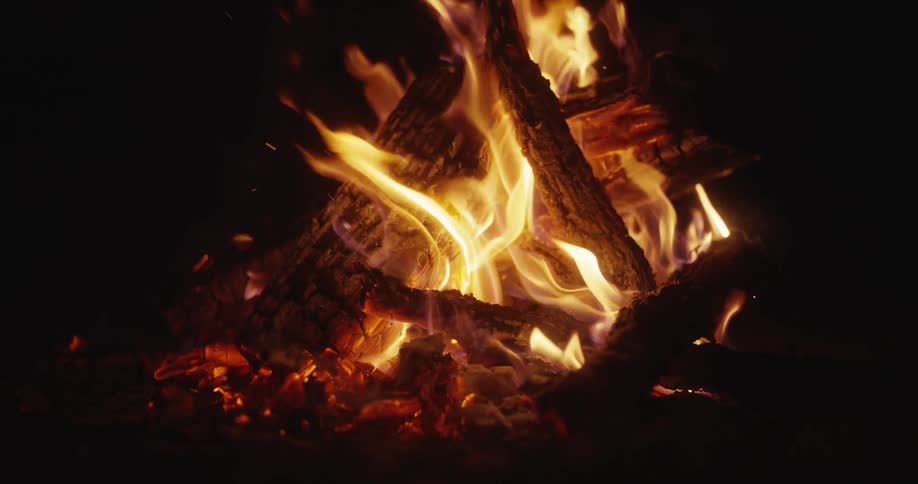 A stick moves the wood of a bonfire as flames rise in the darkness