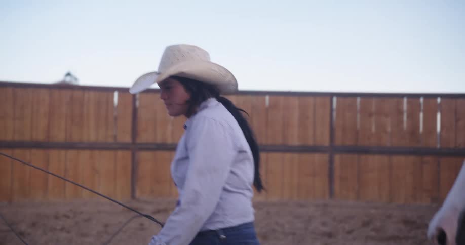 A woman with a rope in her hand and a horse behind her follows
