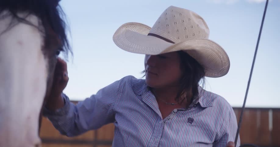 A woman in a cowboy hat is petting a horse