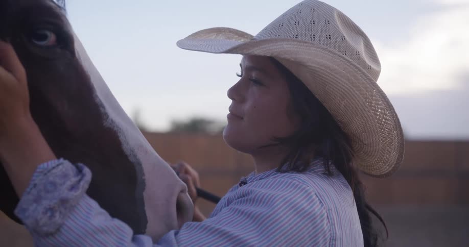 Portrait of a cowgirl caressing the face of a horse