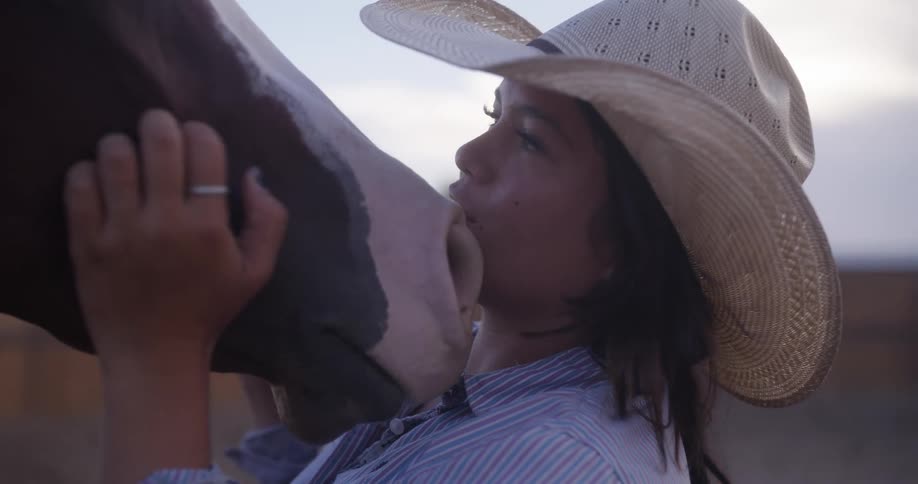 A woman in a cowboy hat kissing and petting a horses face